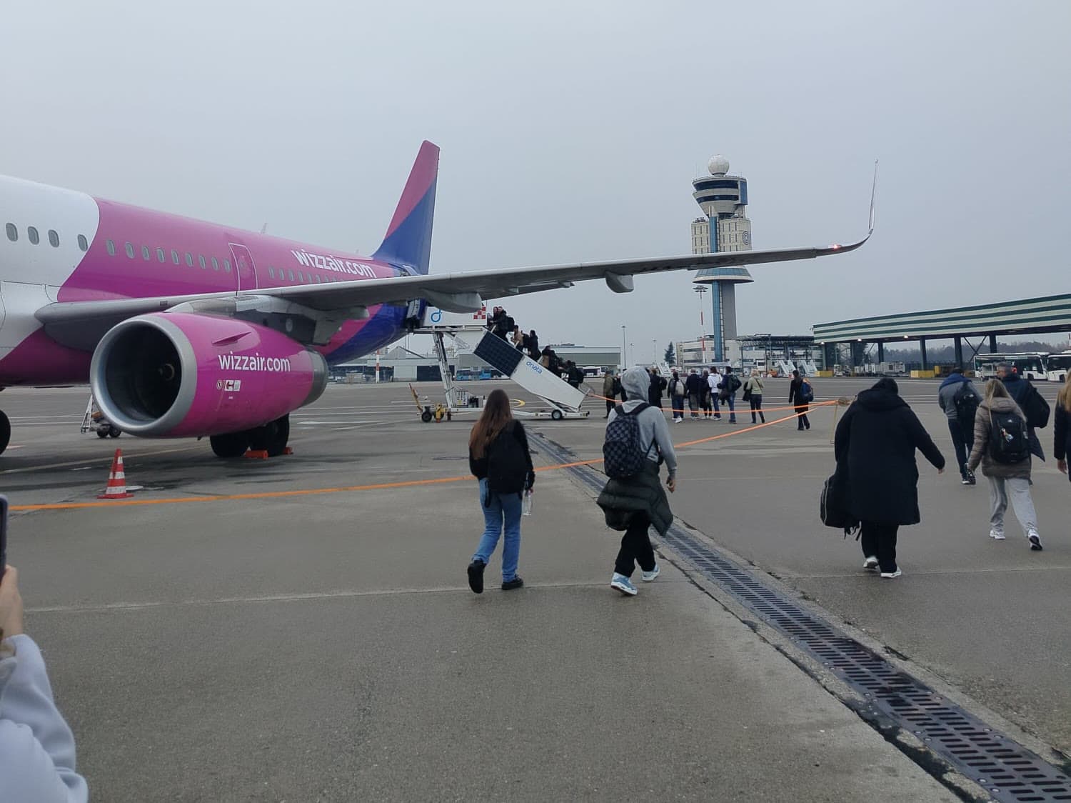 Un aereo fermo in pista e le persone che ci camminano verso, in un aeroporto in una giornata grigia
