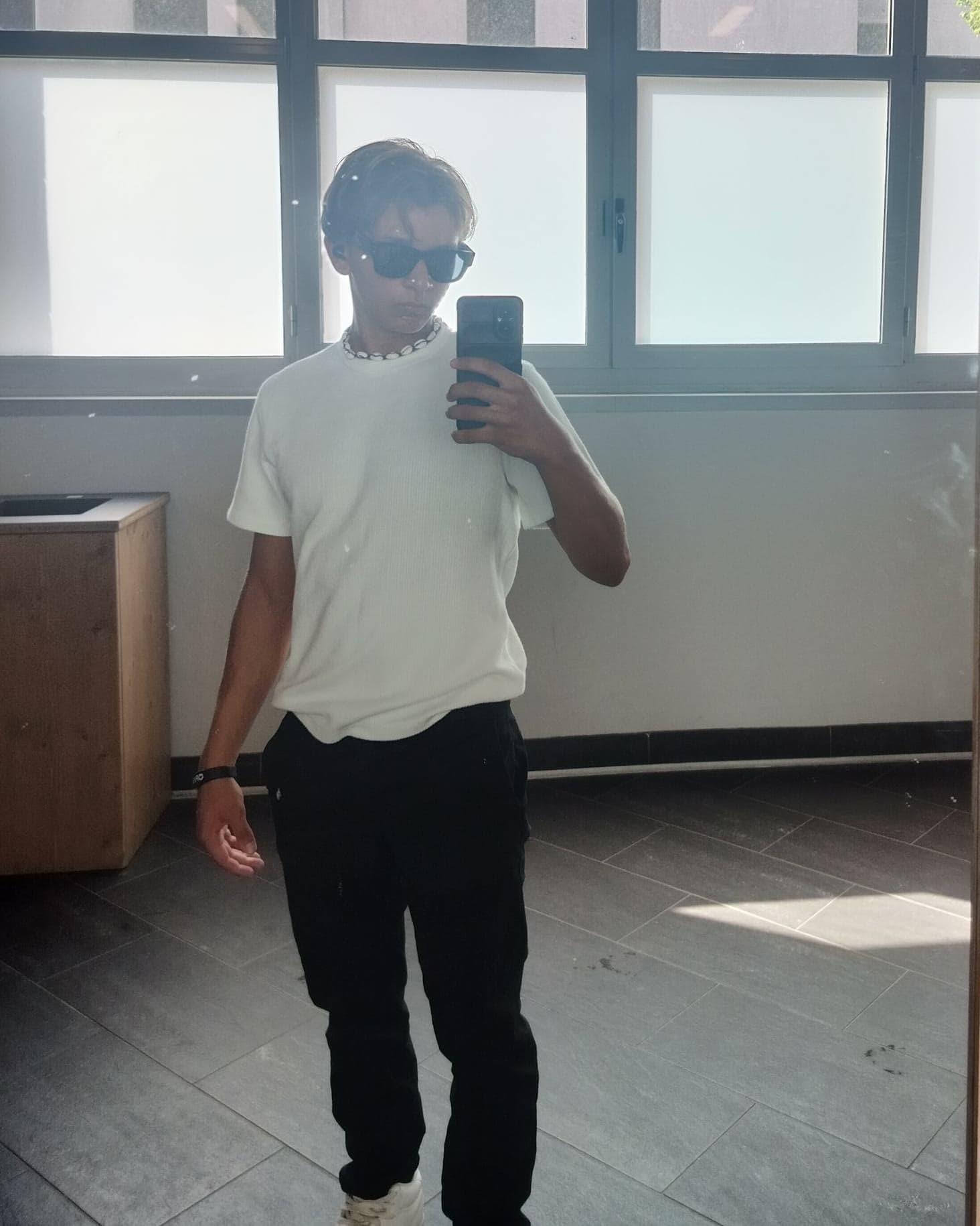 Io allo specchio di un corridoio della scuola, occhiali da sole e telefono in mano