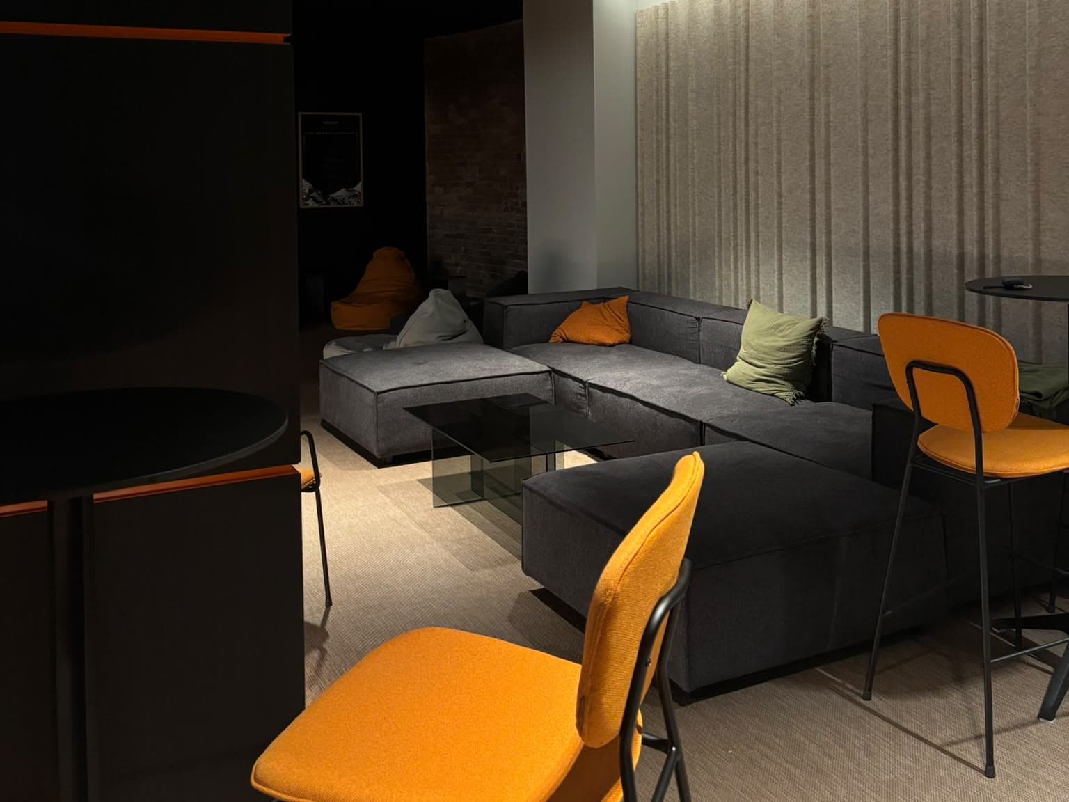 L'angolo lounge di uno spazio di lavoro: divano grigio, sedie arancioni e un tavolino di vetro