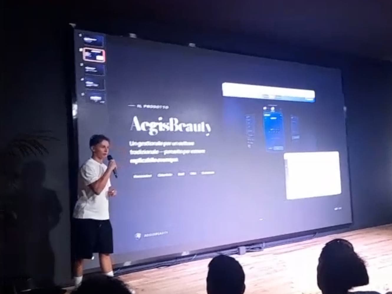 Io sul palco con il microfono, davanti allo schermo che proietta la slide di Aegis Beauty